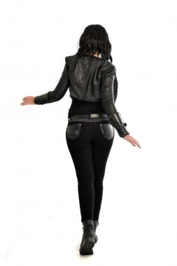 tam uzunlukta uzak kameradan bakan deri kıyafeti giymiş siyah saçlı kız portresi. Beyaz stüdyo arka plan üzerinde ayakta poz.