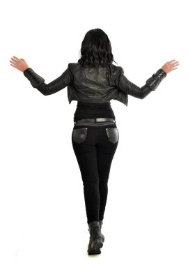 tam uzunlukta uzak kameradan bakan deri kıyafeti giymiş siyah saçlı kız portresi. Beyaz stüdyo arka plan üzerinde ayakta poz.