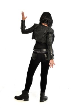 tam uzunlukta uzak kameradan bakan deri kıyafeti giymiş siyah saçlı kız portresi. Beyaz stüdyo arka plan üzerinde ayakta poz.