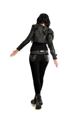 tam uzunlukta uzak kameradan bakan deri kıyafeti giymiş siyah saçlı kız portresi. Beyaz stüdyo arka plan üzerinde ayakta poz.
