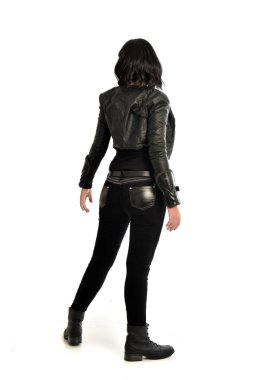 tam uzunlukta uzak kameradan bakan deri kıyafeti giymiş siyah saçlı kız portresi. Beyaz stüdyo arka plan üzerinde ayakta poz.