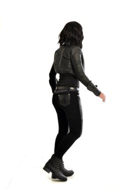 tam uzunlukta uzak kameradan bakan deri kıyafeti giymiş siyah saçlı kız portresi. Beyaz stüdyo arka plan üzerinde ayakta poz.