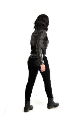 tam uzunlukta uzak kameradan bakan deri kıyafeti giymiş siyah saçlı kız portresi. Beyaz stüdyo arka plan üzerinde ayakta poz.