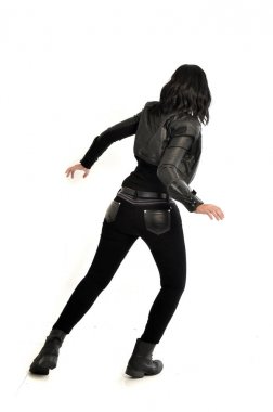 tam uzunlukta uzak kameradan bakan deri kıyafeti giymiş siyah saçlı kız portresi. Beyaz stüdyo arka plan üzerinde ayakta poz.