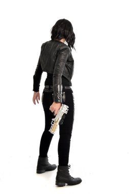 deri kıyafeti giymiş siyah saçlı kız tam uzunlukta portresi. bir beyaz stüdyo arka plan üzerinde izole bir silah tutarken ayakta poz.