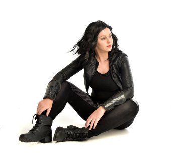 deri kıyafeti giymiş siyah saçlı kız tam uzunlukta portresi. poz, beyaz stüdyo arka plan üzerinde izole üzerinde oturmuş.