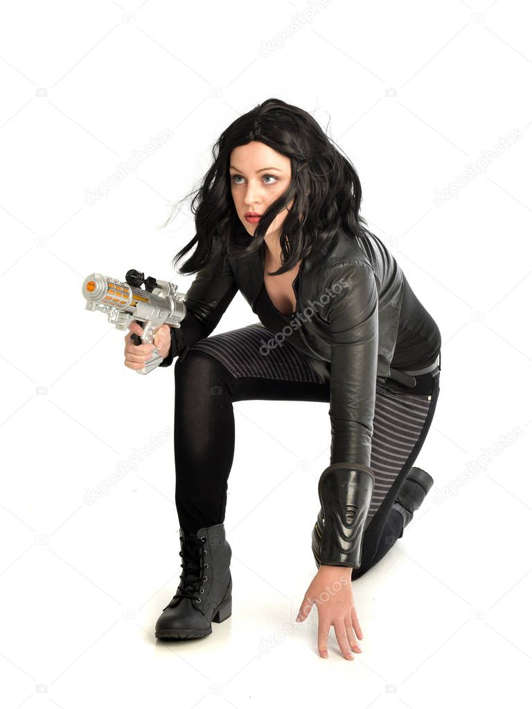 full length portrait of black haired girl wearing leather outfit.  seated on pose, isolated on a white studio background.