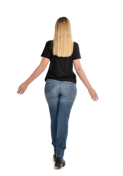 シンプルな黒シャツとジーンズを身に着けているブロンドの女の子の完全な長さの肖像画 白い背景で隔離のカメラから離れて直面して立ちポーズ — ストック写真