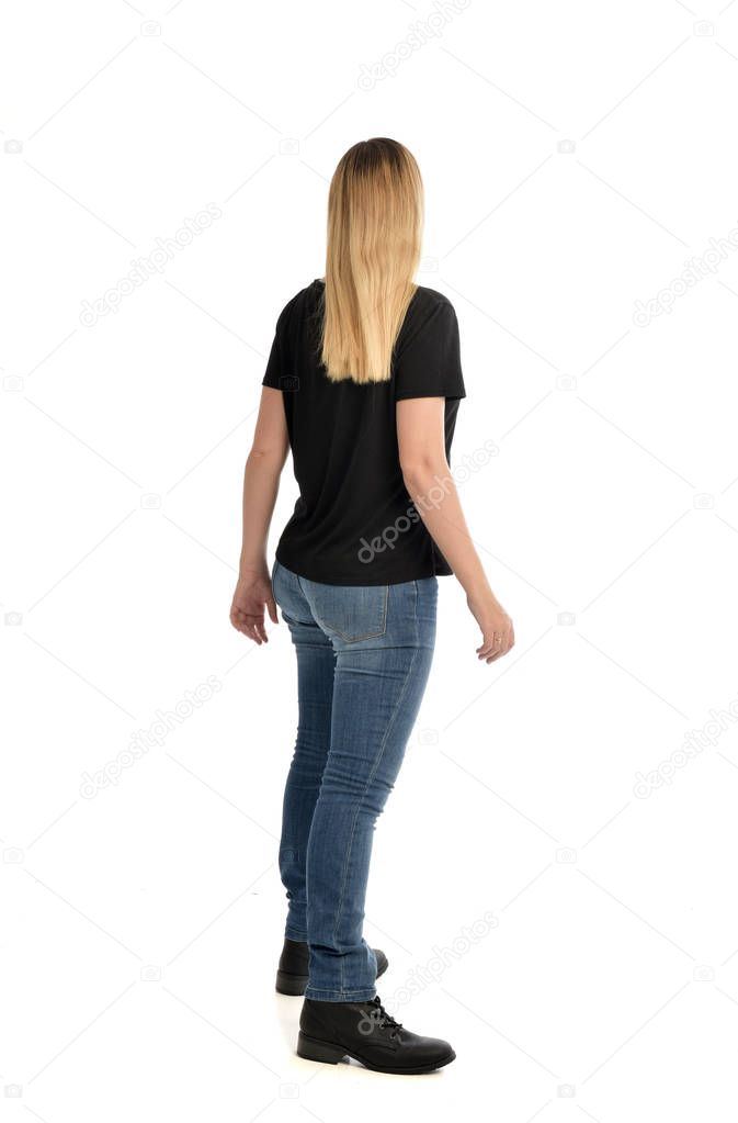 full length portrait of blonde girl wearing simple black shirt and jeans. standing pose facing away from camera, isolated on white background.