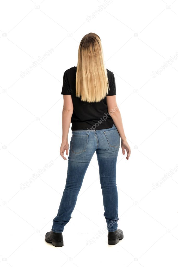 full length portrait of blonde girl wearing simple black shirt and jeans. standing pose facing away from camera, isolated on white background.