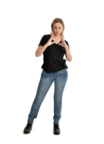 基本的な黒の シャツとジーンズを身に着けているブロンドの女の子は 白い背景の上の立ちポーズの完全な長さの肖像画 — ストック写真