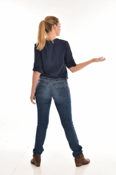 全长的肖像金发女郎身穿简单的蓝色衬衫和牛仔裤 站立姿势面对远离相机 在白色背景上隔离 — 图库照片