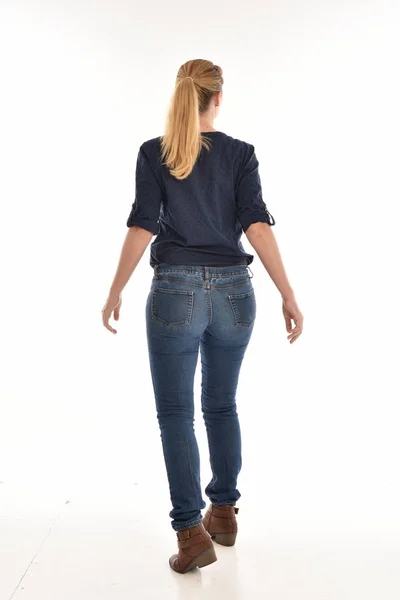 全长的肖像金发女郎身穿简单的蓝色衬衫和牛仔裤 站立姿势面对远离相机 在白色背景上隔离 — 图库照片