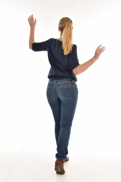 カメラから離れて直面しているポーズに立っているシンプルなブルーのシャツとジーンズを身に着けている金髪の女の子の完全な長さの肖像画 白い背景に分離 — ストック写真