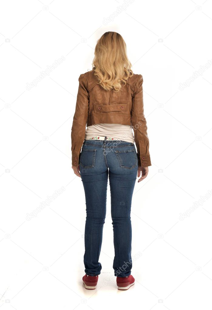 full length portrait of blonde girl wearing brown jacket and jeans. standing pose on white background.