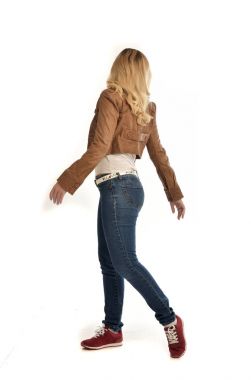 tam uzunlukta portre sarışın kız kahverengi ceket ve kot pantolon giyiyor. Beyaz arka plan üzerinde ayakta poz.
