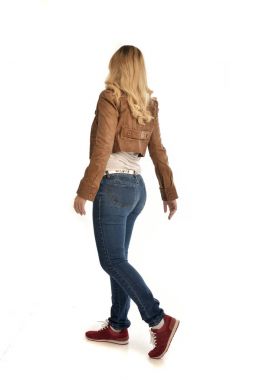 tam uzunlukta portre sarışın kız kahverengi ceket ve kot pantolon giyiyor. Beyaz arka plan üzerinde ayakta poz.