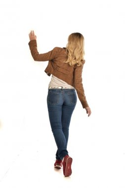 tam uzunlukta portre sarışın kız kahverengi ceket ve kot pantolon giyiyor. Beyaz arka plan üzerinde ayakta poz.