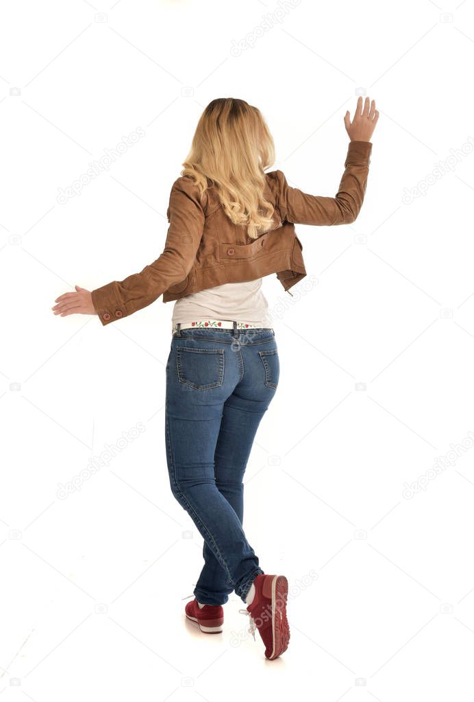 full length portrait of blonde girl wearing brown jacket and jeans. standing pose on white background.