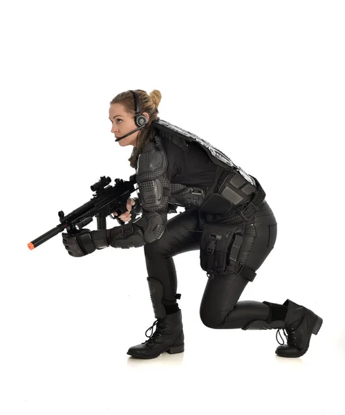 女性の黒の戦術的な鎧 しゃがみポーズを身に着けている白いスタジオ背景に分離した武器を持ちの完全な長さの肖像画 — ストック写真