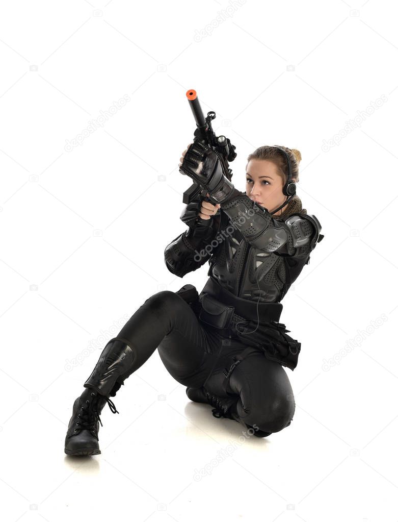 full length portrait of female wearing black  tactical armour, crouching pose and holding a weapon, isolated on white studio background.