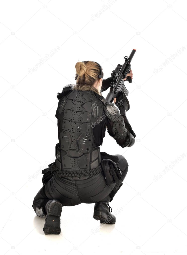 full length portrait of female wearing black  tactical armour, crouching pose and holding a weapon, isolated on white studio background.