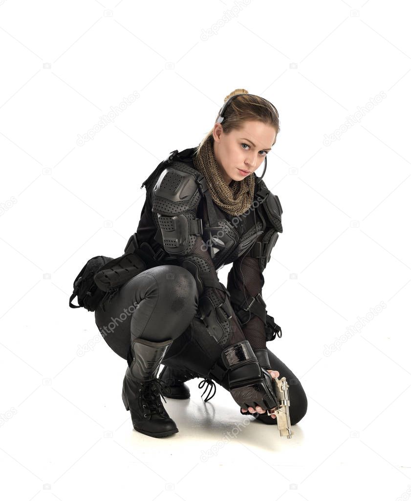 full length portrait of female wearing black  tactical armour, crouching pose and holding a weapon, isolated on white studio background.
