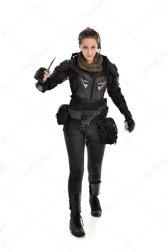 full length portrait of female  soldier wearing black  tactical armour, holding a knife, isolated on white studio background.