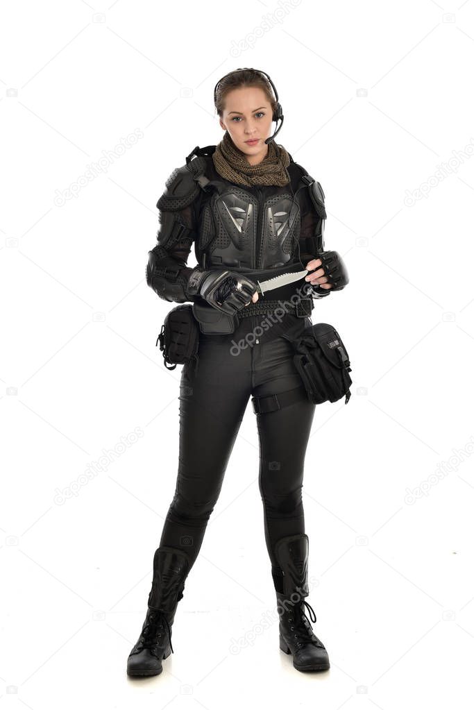 full length portrait of female  soldier wearing black  tactical armour, holding a knife, isolated on white studio background.