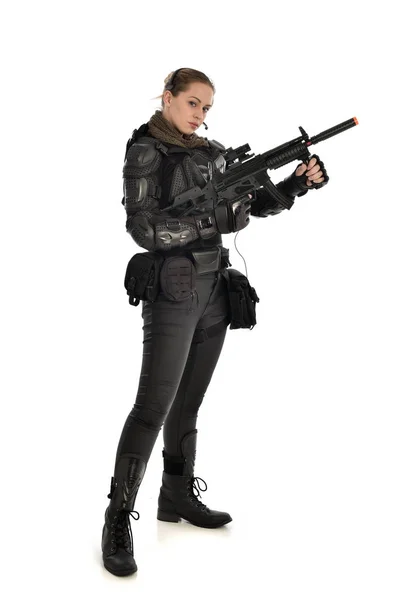 戦術的な黒の鎧を着て 白いスタジオ背景に分離されたライフル銃を保持している女性兵士の完全な長さの肖像画 — ストック写真