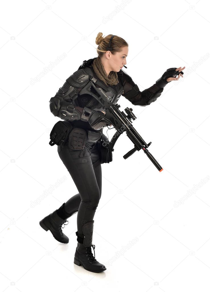 full length portrait of female  soldier wearing black  tactical armour, holding a rifle gun, isolated on white studio background.