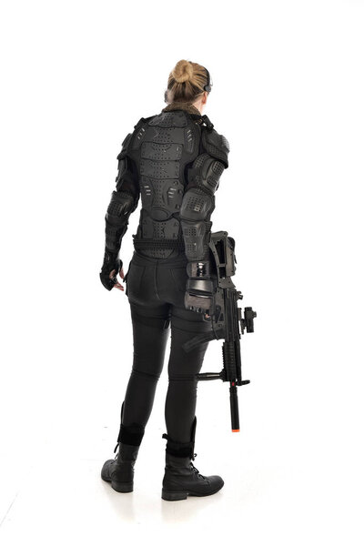 портрет женщины-солдата в чёрных тактических доспехах, держащей винтовку, изолированный на белом фоне студии
.