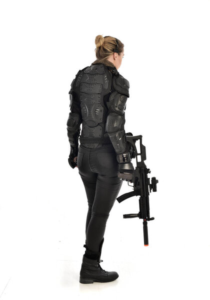 full length portrait of female  soldier wearing black  tactical armour, holding a rifle gun, isolated on white studio background.