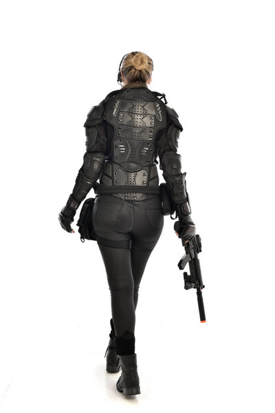 портрет женщины-солдата в чёрных тактических доспехах, держащей винтовку, изолированный на белом фоне студии
.