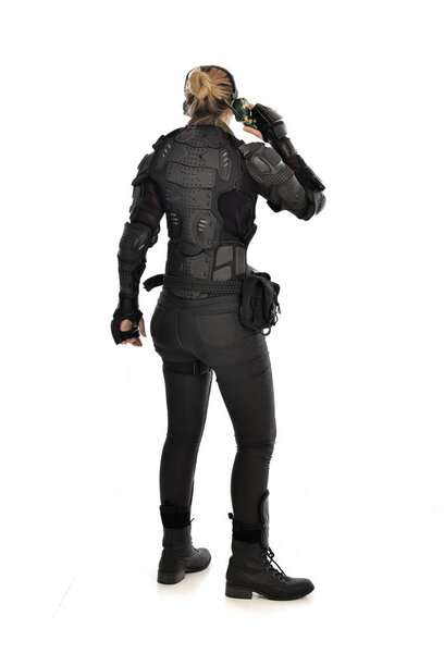 портрет женщины-солдата в чёрных тактических доспехах, стоящей спиной к камере с рацией, изолированной на белом фоне студии
.