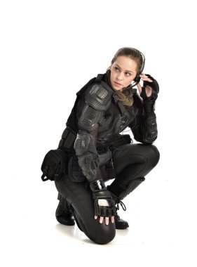 tam uzunlukta izole beyaz stüdyo arka plan üzerinde siyah taktik zırh, oturmuş poz, giyen kadın asker portresi.