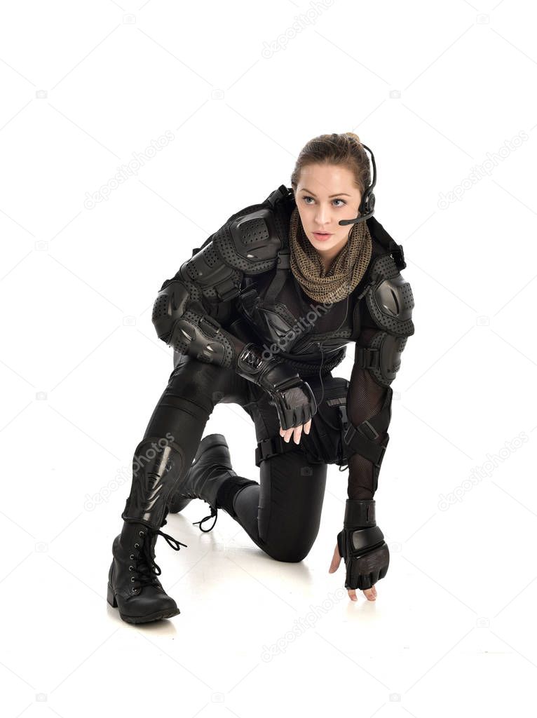 full length portrait of female  soldier wearing black  tactical armour, seated pose, isolated on white studio background.