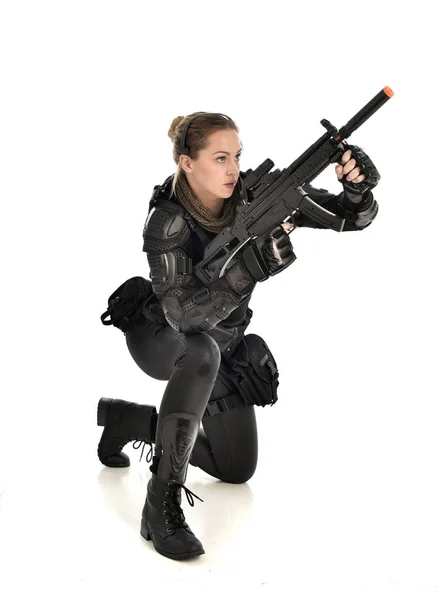 身穿黑色战术盔甲的女士兵全长画像 坐着一把枪 在白色工作室背景下孤立的姿势 — 图库照片