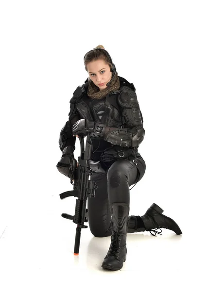 身穿黑色战术盔甲的女士兵全长画像 坐着一把枪 在白色工作室背景下孤立的姿势 — 图库照片