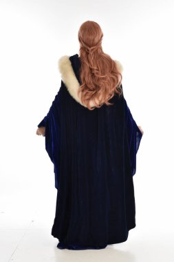 tam uzunlukta bir mavi kadife Ortaçağ elbisesi ve kürk Pelerin giyen kadın uzun saçlı portresi. arka beyaz arka plan üzerinde izole kamera ile ayakta poz.