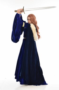tam uzunlukta bir mavi kadife Ortaçağ elbisesi ve kürk Pelerin giyen kadın uzun saçlı portresi. arka beyaz arka plan üzerinde izole kamera ile ayakta poz.