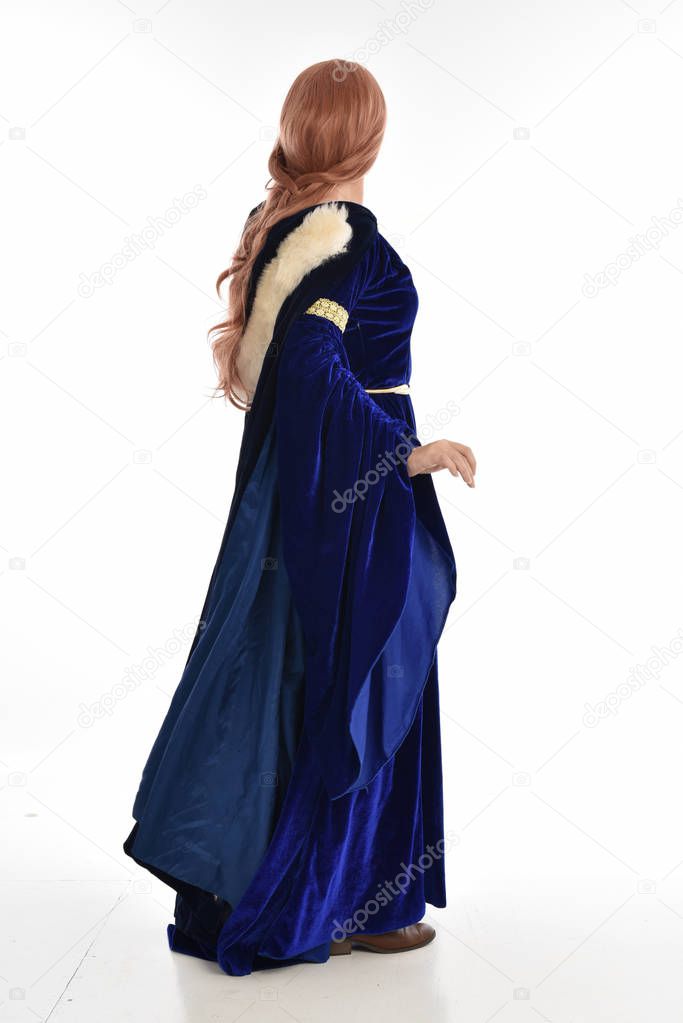 full length portrait of woman with long hair, wearing a blue velvet medieval gown and fur cloak. standing pose with back to the camera, isolated on white background.