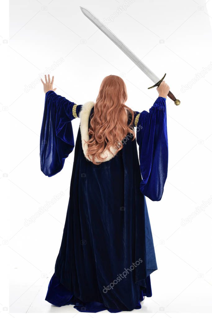 full length portrait of woman with long hair, wearing a blue velvet medieval gown and fur cloak. standing pose with back to the camera, isolated on white background.