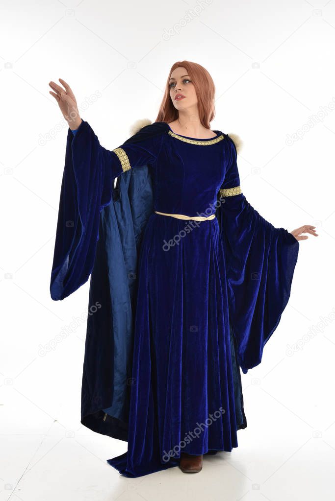 full length portrait of woman with long hair, wearing a blue velvet medieval gown and fur cloak. standing pose, isolated on white background.