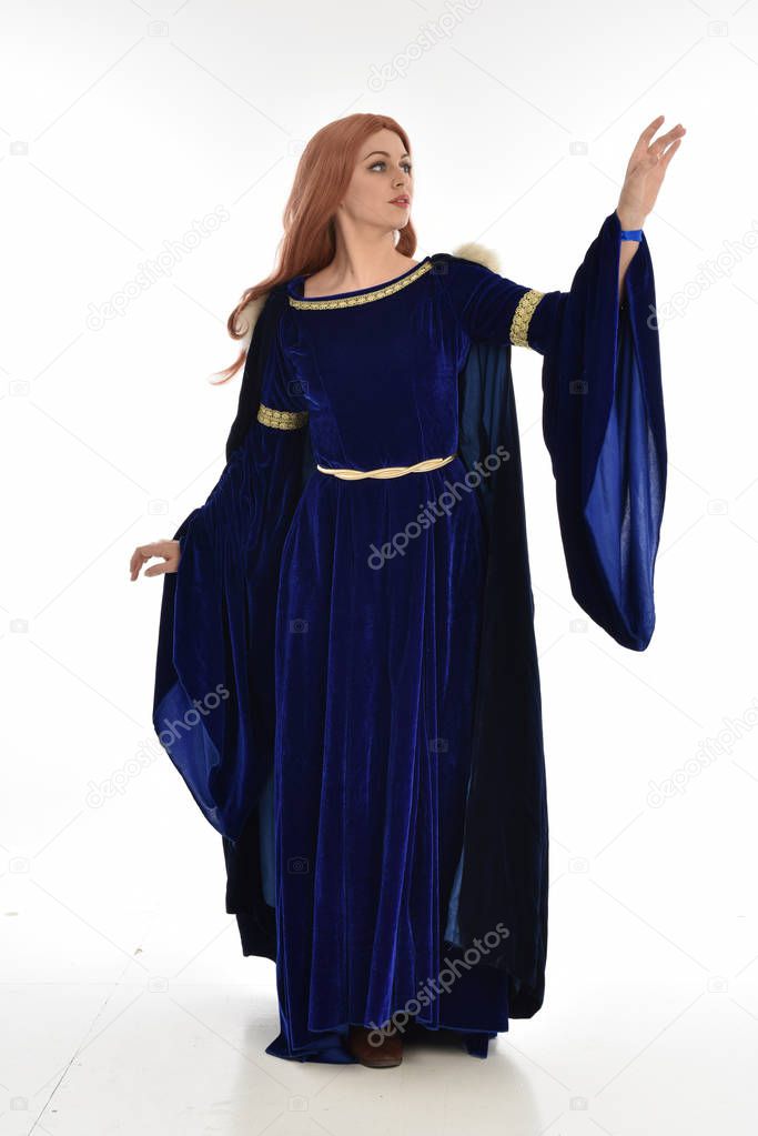 full length portrait of woman with long hair, wearing a blue velvet medieval gown and fur cloak. standing pose, isolated on white background.