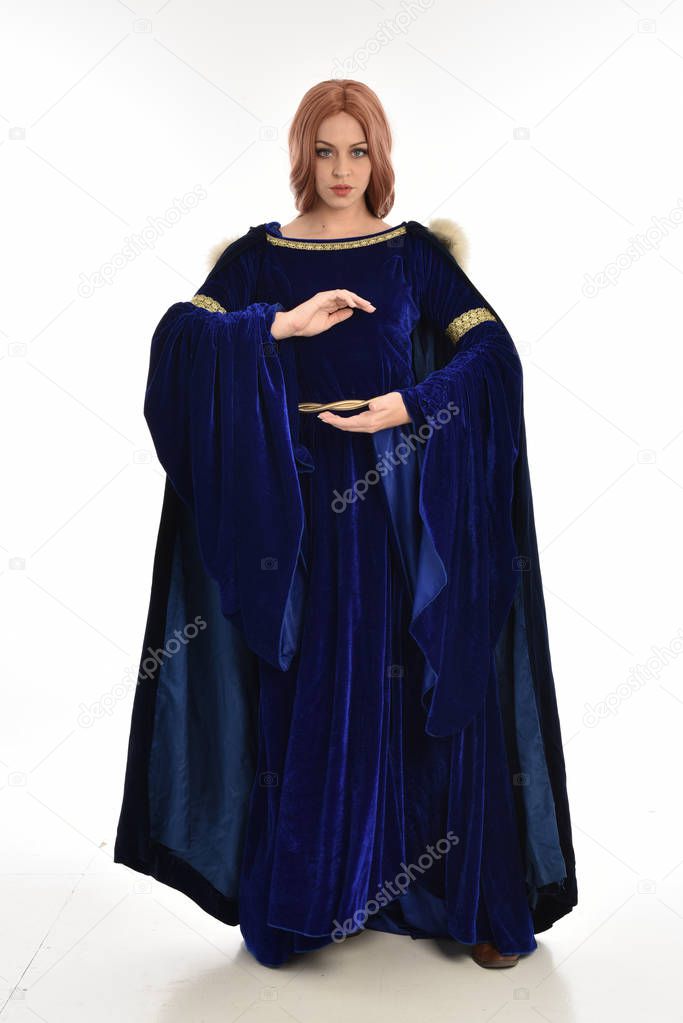 full length portrait of woman with long hair, wearing a blue velvet medieval gown and fur cloak. standing pose, isolated on white background.