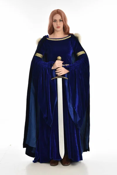 ブルー ベルベット中世のガウンと毛皮のマントを着た長い髪の女性の完全な長さの肖像画 立ちは 白い背景で隔離 長い剣を持ったポーズします — ストック写真