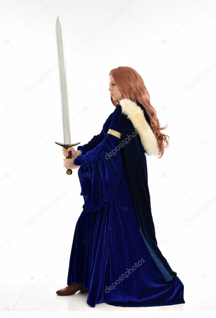 full length portrait of woman with long hair, wearing a blue velvet medieval gown and fur cloak. standing pose in side profile, isolated on white background.