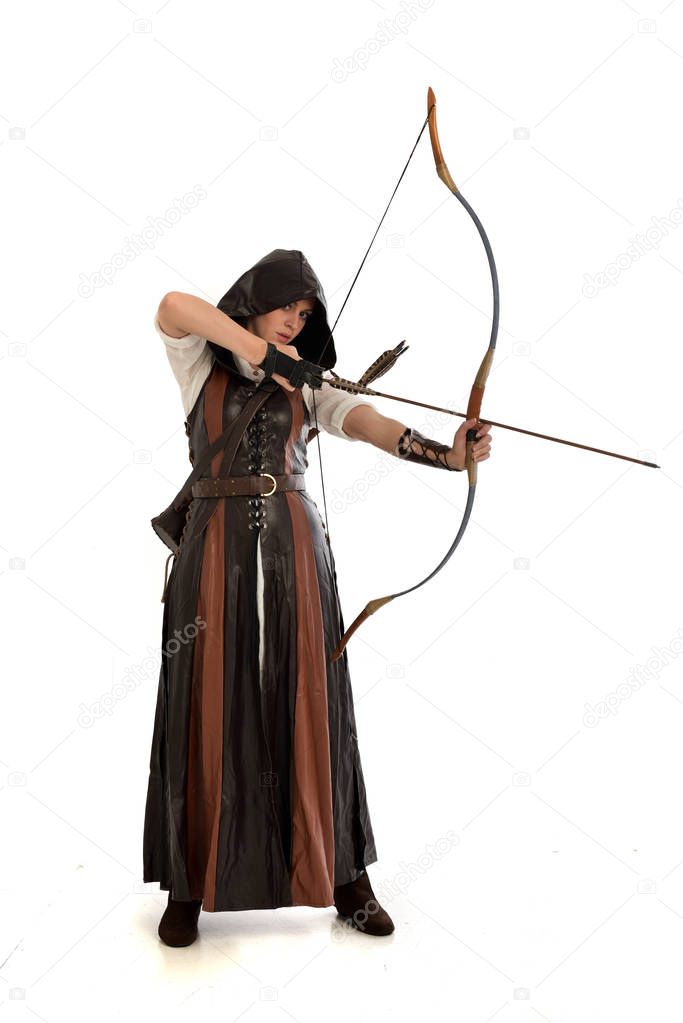 full length portrait of woman wearing brown medieval fantasy outfit, with a bow and arrow. standing pose on white studio background.