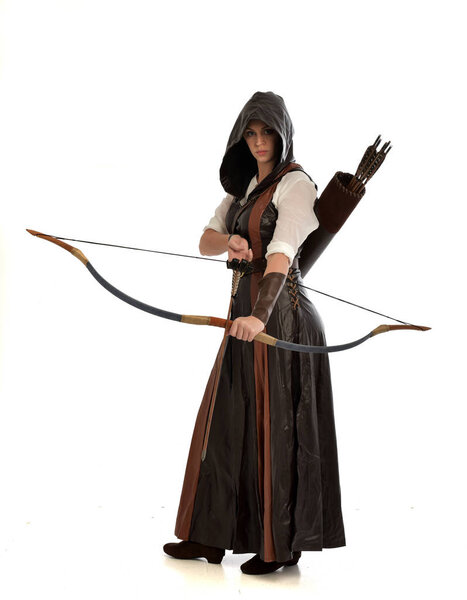 full length portrait of woman wearing brown medieval fantasy outfit, with a bow and arrow. standing pose on white studio background.